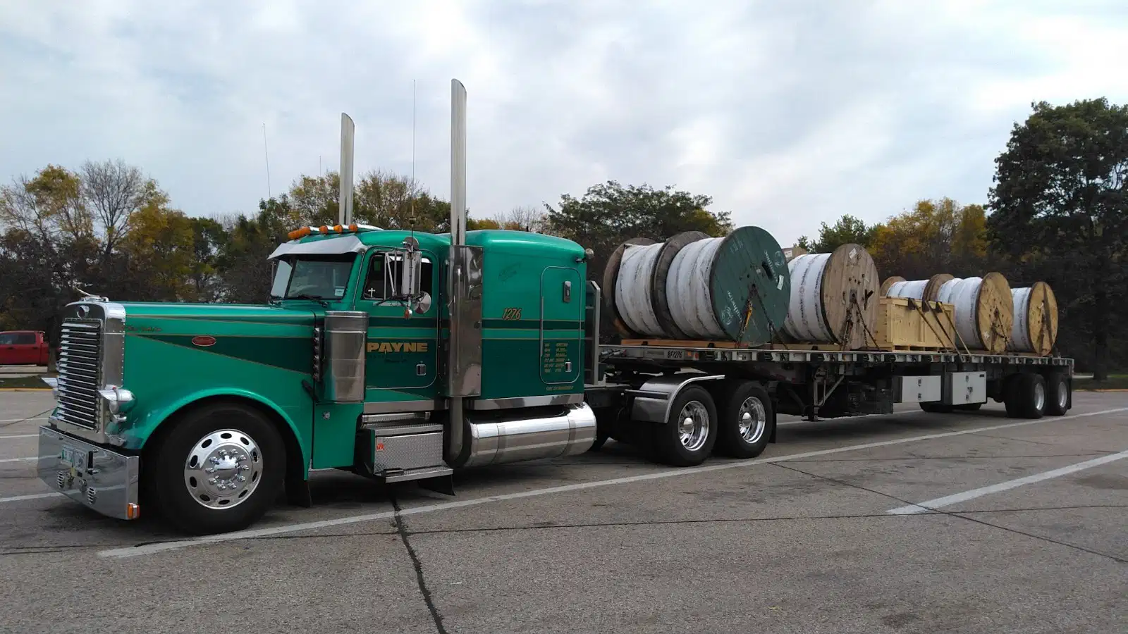 Payne semi-truck hauling large cable reels on a flatbed trailer.